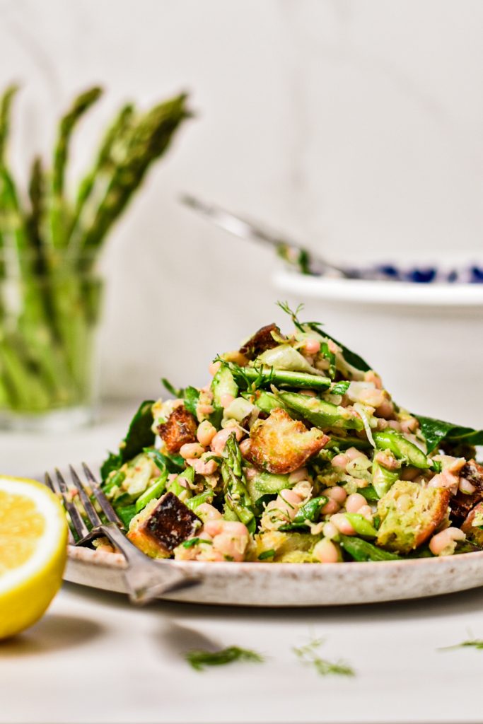 Side view of raw asparagus white bean tuna salad piled high on a plate next to a fork.
