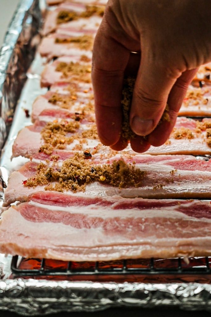 Hand sprinkling a sugar and spice mixture on top of the bacon before baking it.