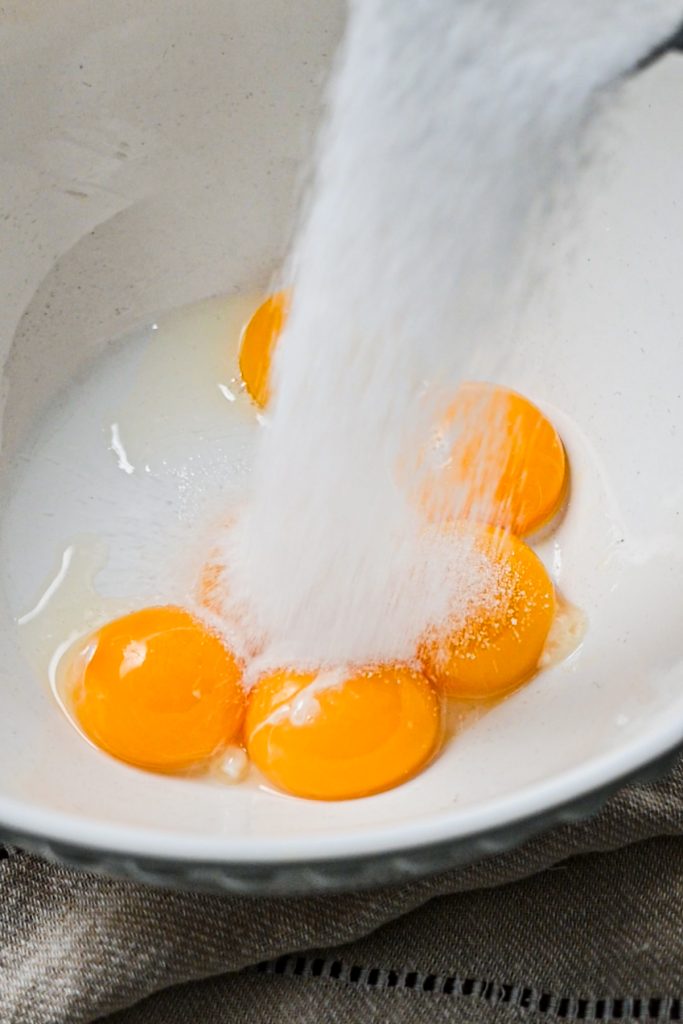 Adding sugar into a bowl of egg yolks.