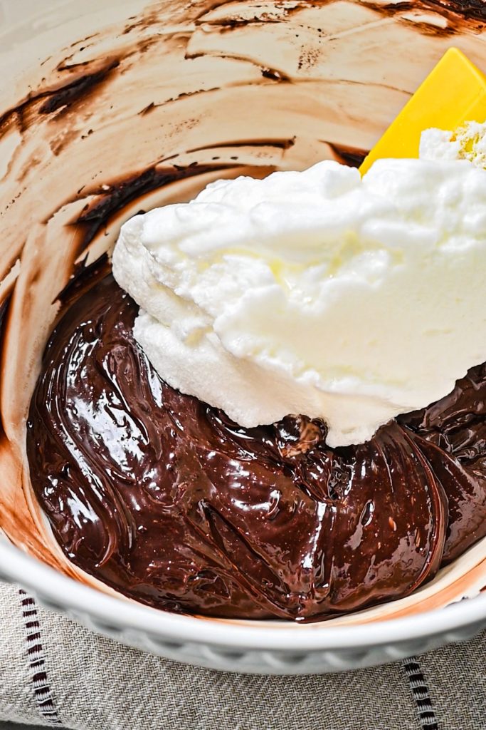 Using a rubber spatula to fold in the fluffy egg whites into the chocolate egg yolk mixture.