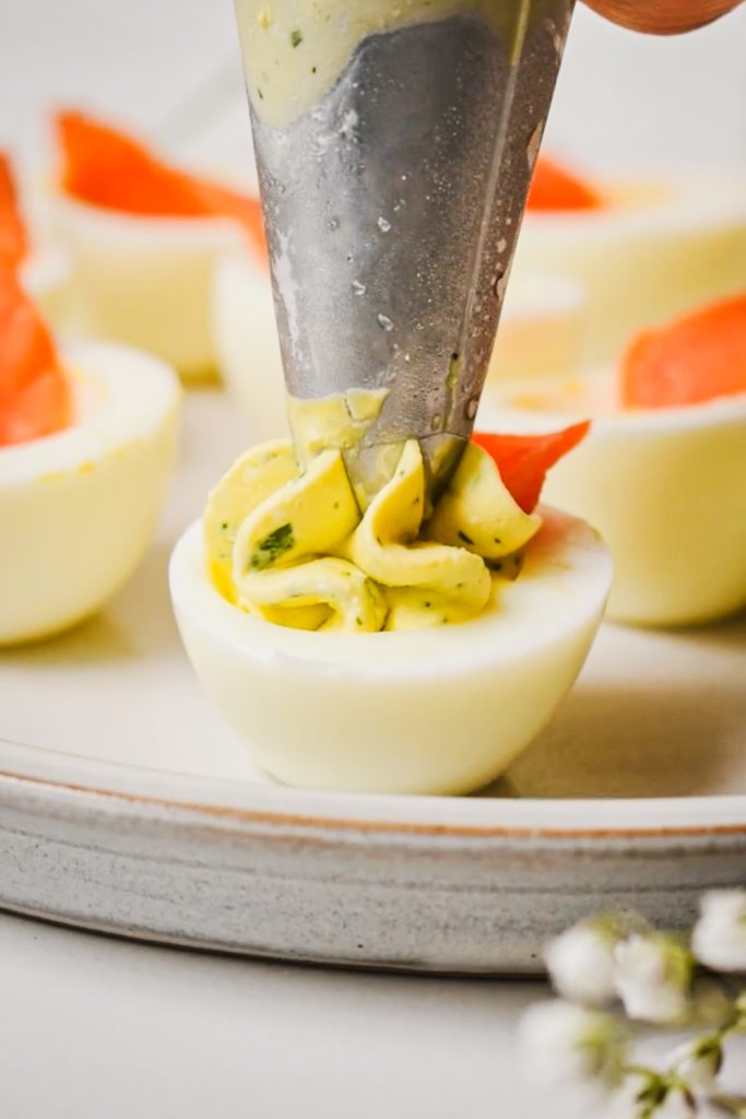 Using a piping bag with a tip to fill the egg whites with the egg yolk filling.