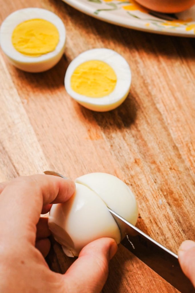 Slicing the hard boiled eggs in half on a wooden board.