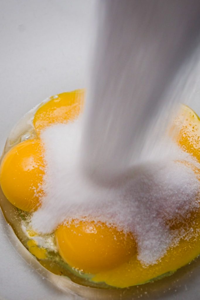 Egg yolks and sugar in a glass mixing bowl.