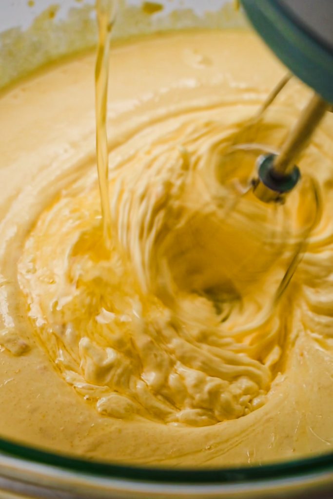 Melted butter being added into the fluffy egg yolk and sugar mixture in a bowl with a mixer.