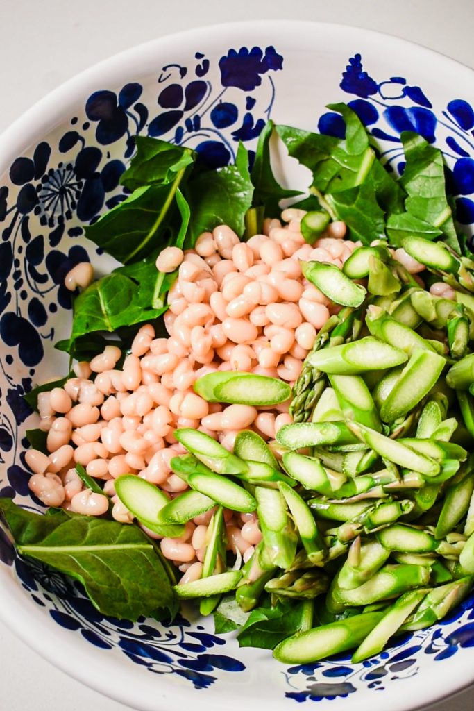 White beans, greens, and sliced asparagus in a large bowl.