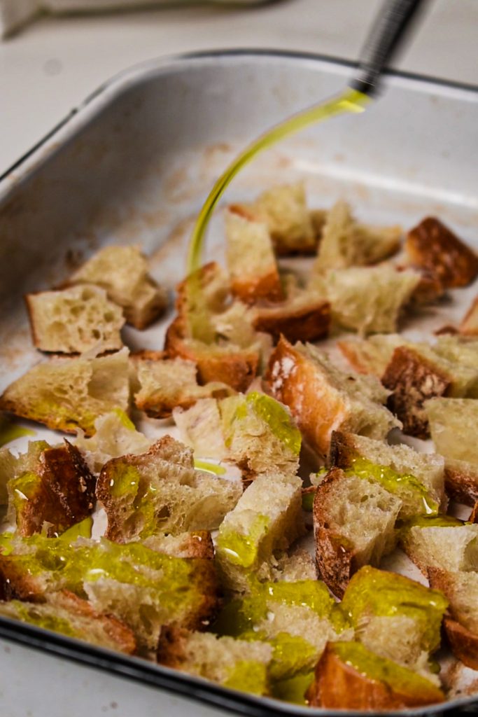 Drizzling olive oil over stale bread cubes in a baking dish.