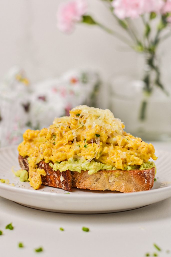Creamy eggs with cottage cheese on a piece of avocado toast topped with parmesan.