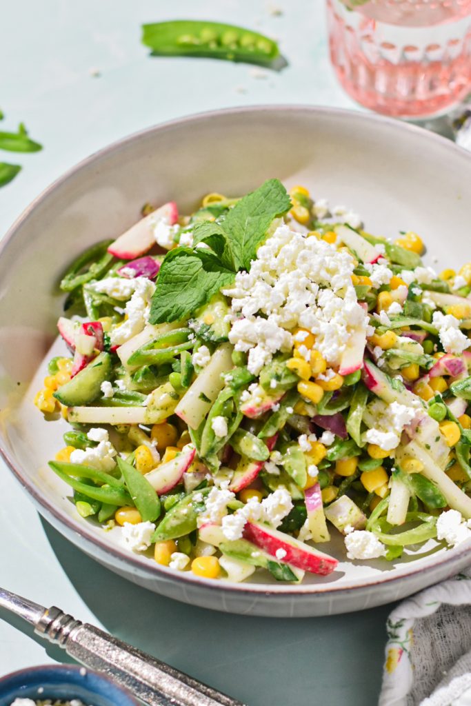 Close up of a serving of sugar snap pea salad in a bowl with feta on top.