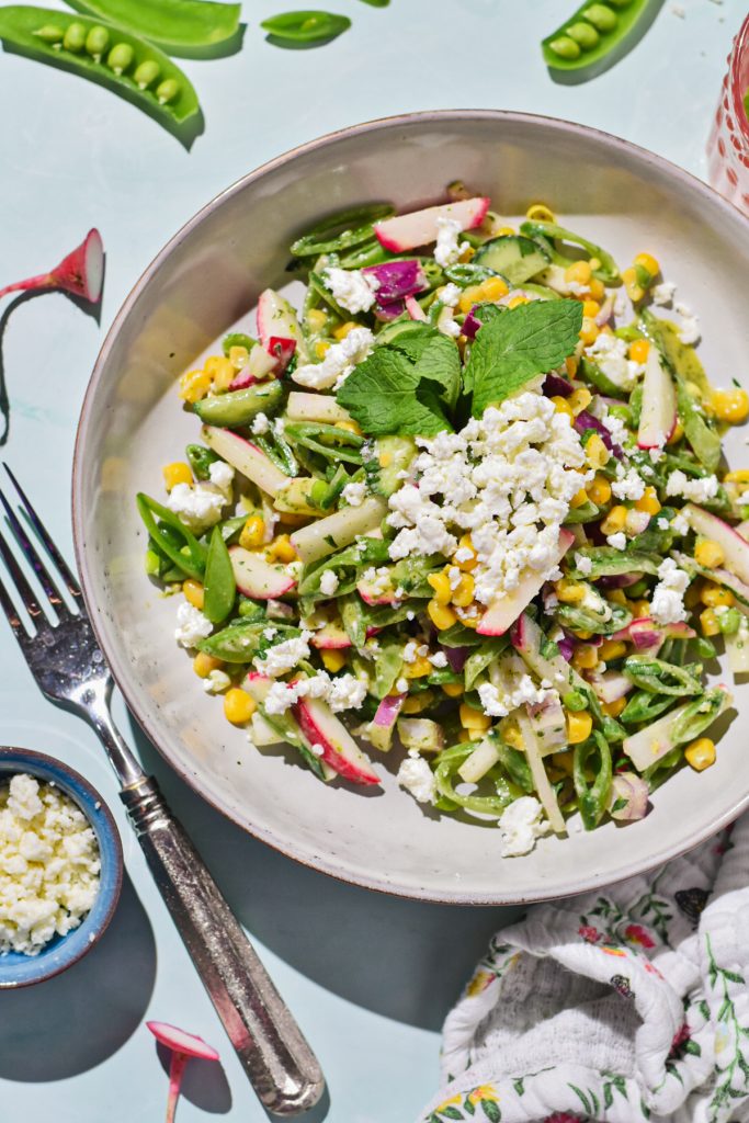 Overhead shot of sugar snap pea salad in a bowl topped with mint and feta.