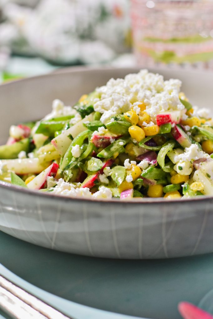 Side view of a fresh sugar snap pea salad with feta in a shallow bowl.