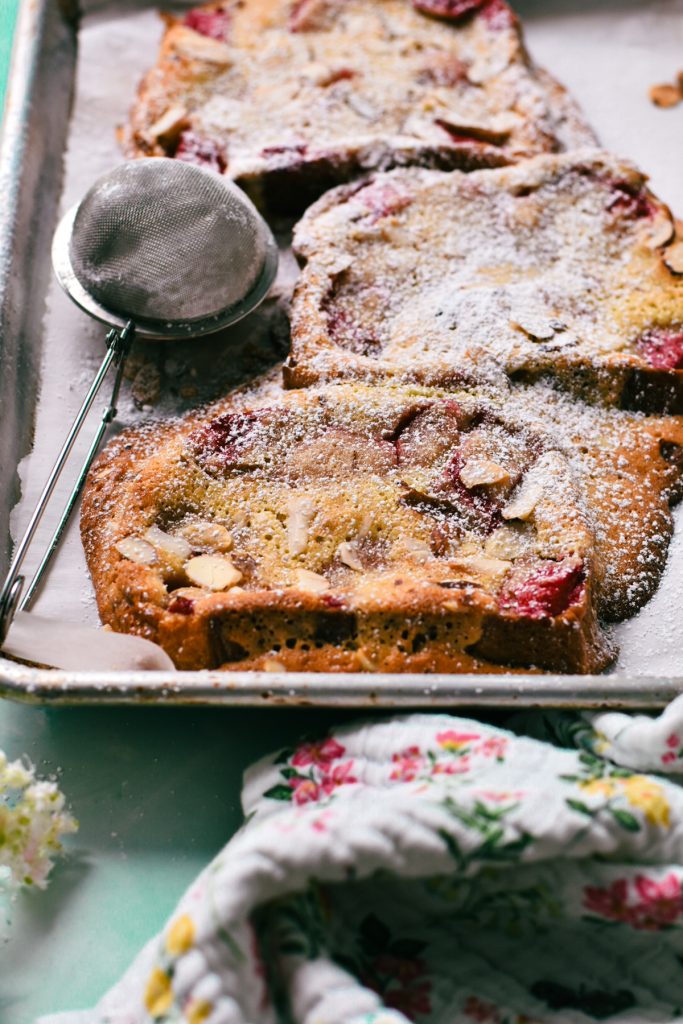 Side view of bostock with rhubarb compote on a sheet pan with powdered sugar on top.