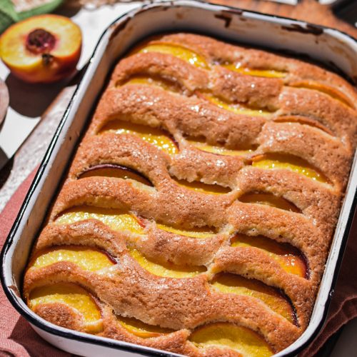 Summer peach cake in the rectangular cake pan on a wooden board.