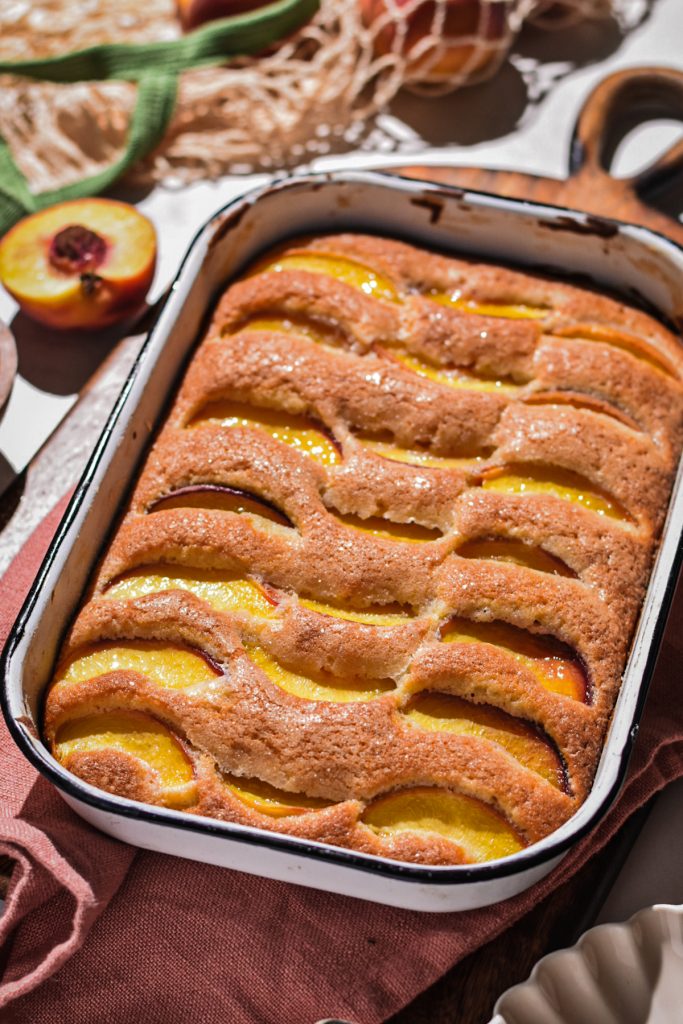 Summer peach cake in the rectangular cake pan on a wooden board.