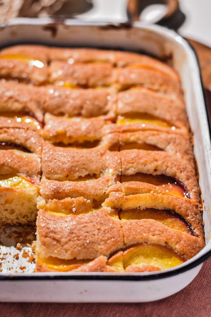 Side view of sliced summer peach cake in the cake pan with one slice missing.