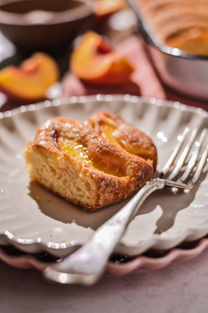 Slice of summer peach cake on a fluted grey plate with a fork.
