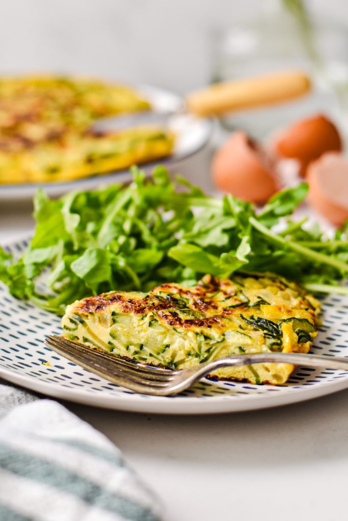 Slice of zucchini tortilla on a plate with a green salad on the side.