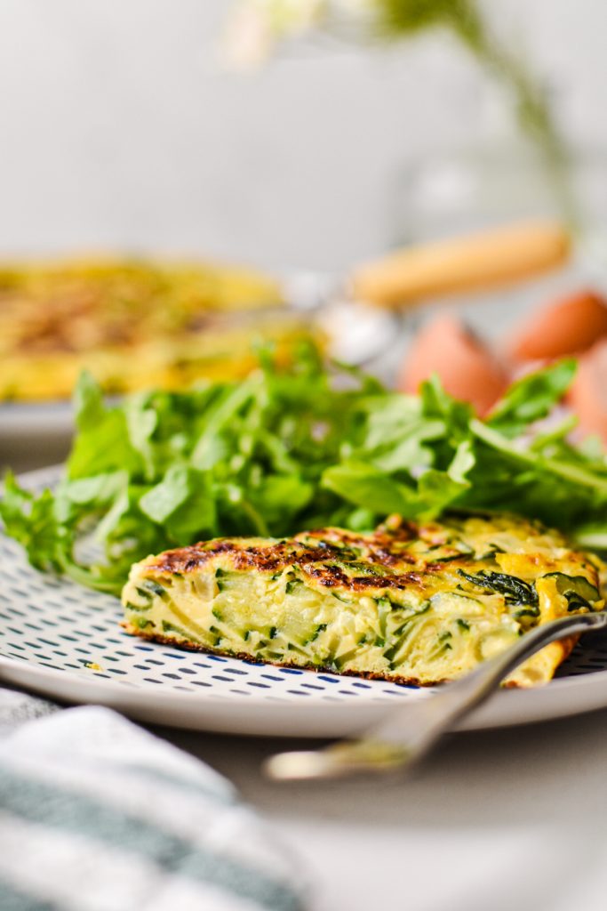 Side view of a slice of zucchini tortilla de patatas on a plate with a green salad on the side.