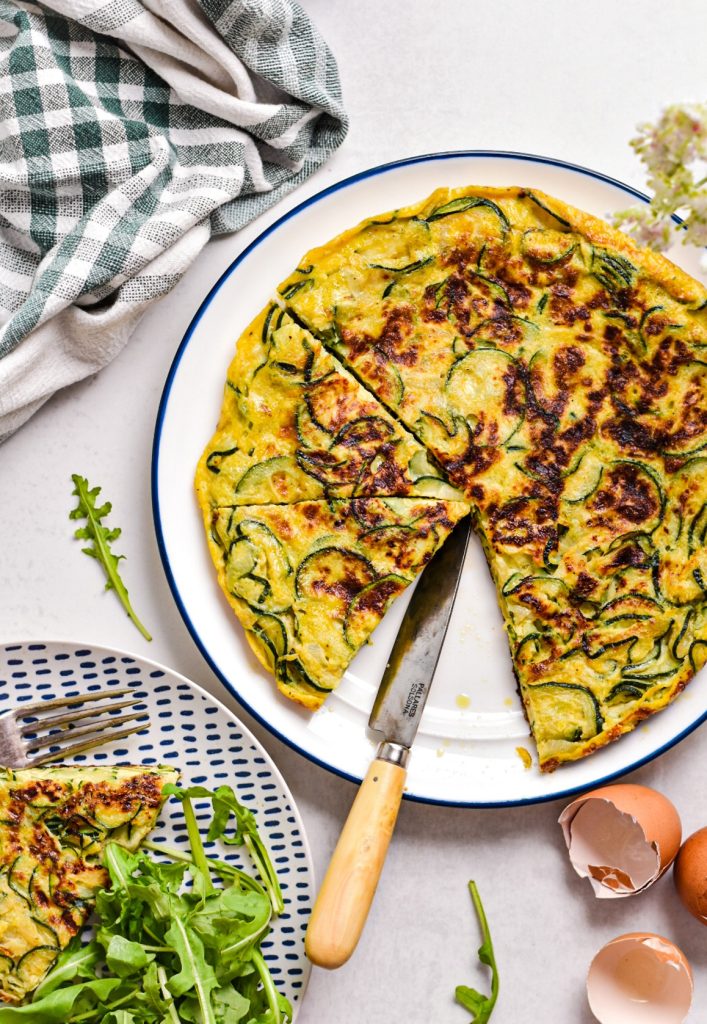 Overhead shot of zucchini tortilla with some of it cut into slices.