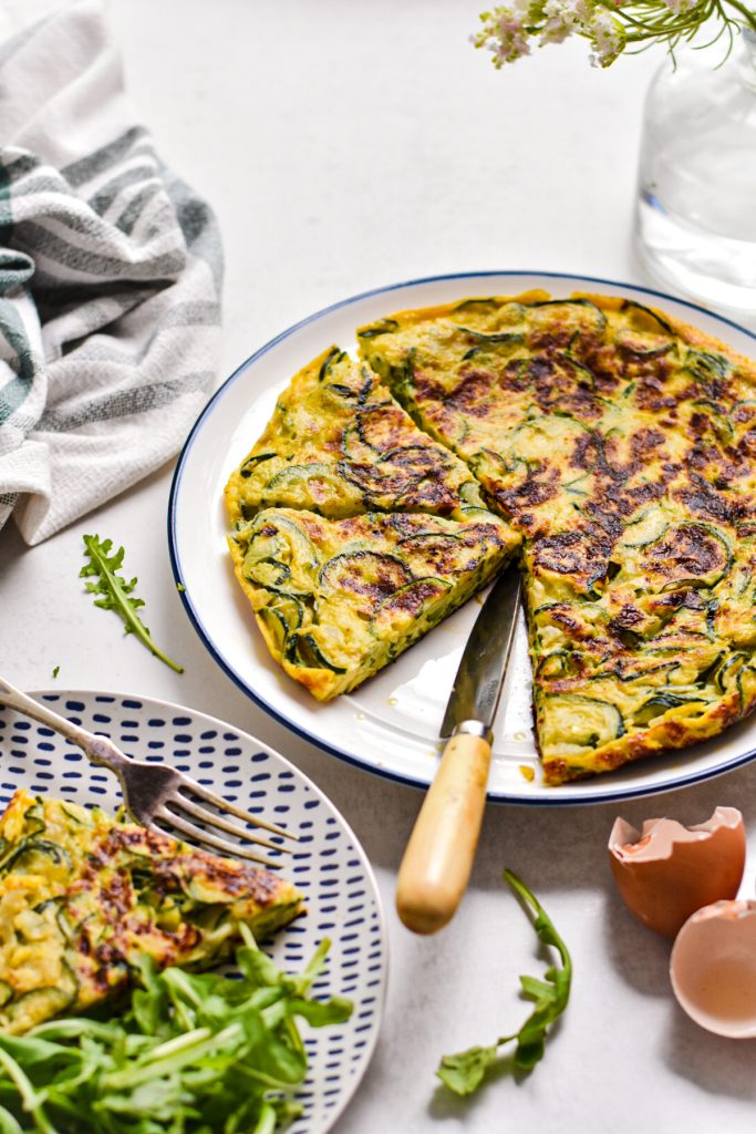 Zucchini tortilla de patatas on a plate next to a plate with a slice and salad on it.