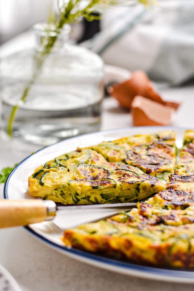 Side view of zucchini tortilla on a plate with a slice missing to see the inside layer.