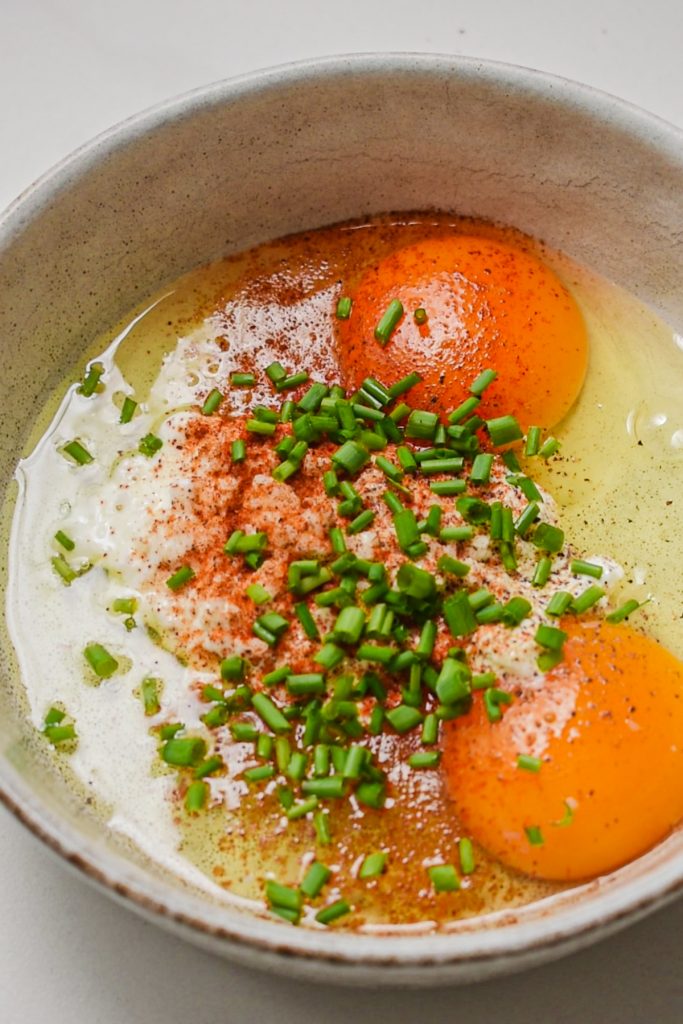 Eggs in a bowl with cottage cheese, spices, and chives.