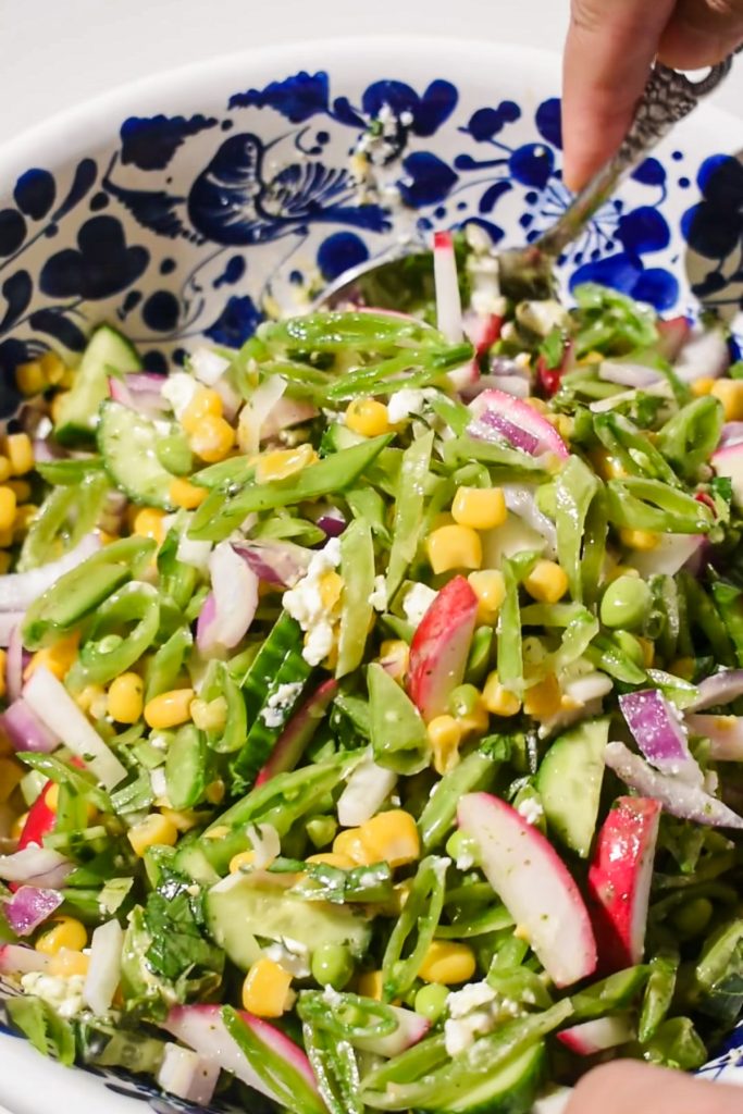 Tossing the snap pea salad with two spoons in a large bowl.
