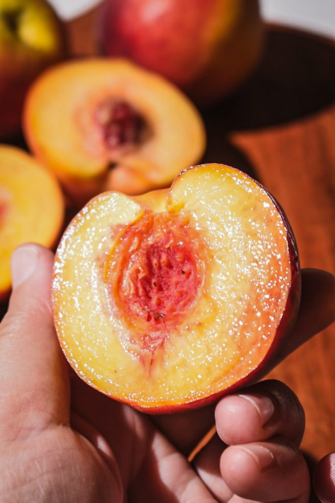 Hand holding a half of a peach with the pit removed.