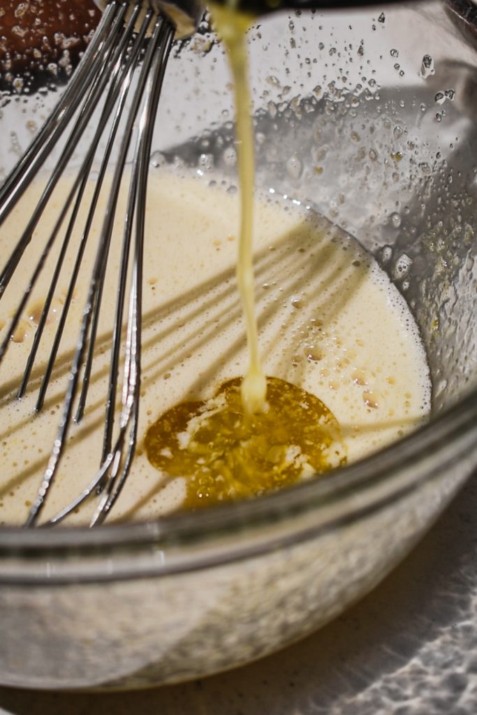 Adding melted butter and extracts to the egg and sugar mixture in a bowl.