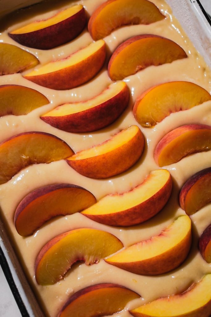 Peach cake batter in a cake pan with fresh peach slices on top.