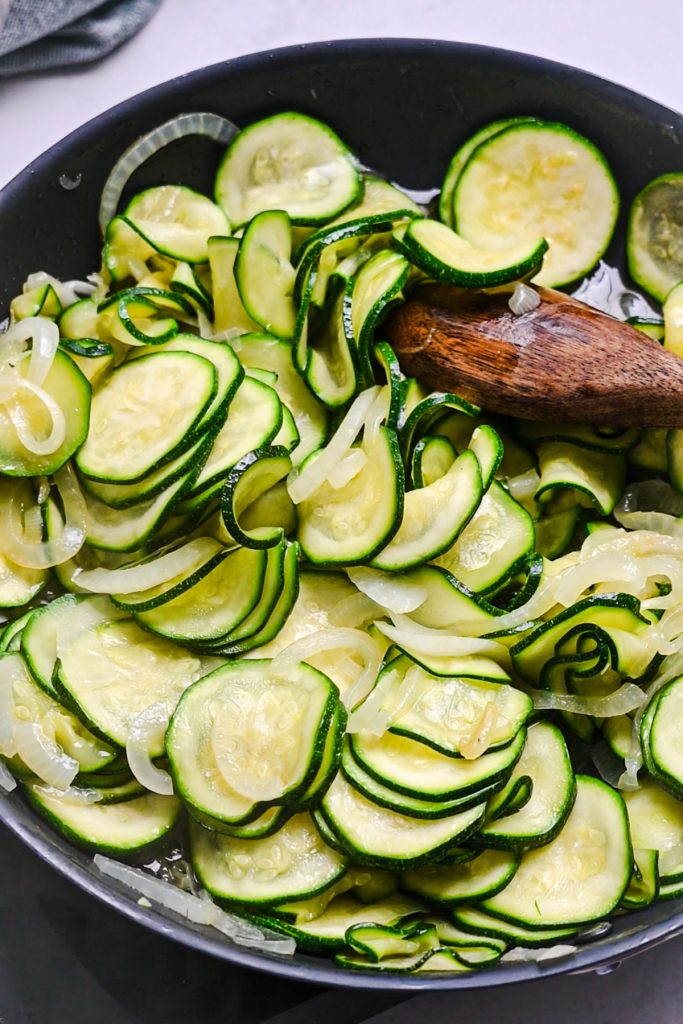Sliced zucchini cooking in the skillet with the onions.