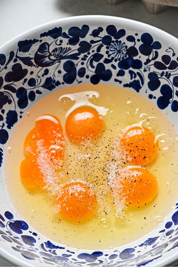 Eggs in a mixing bowl with salt and pepper on top.