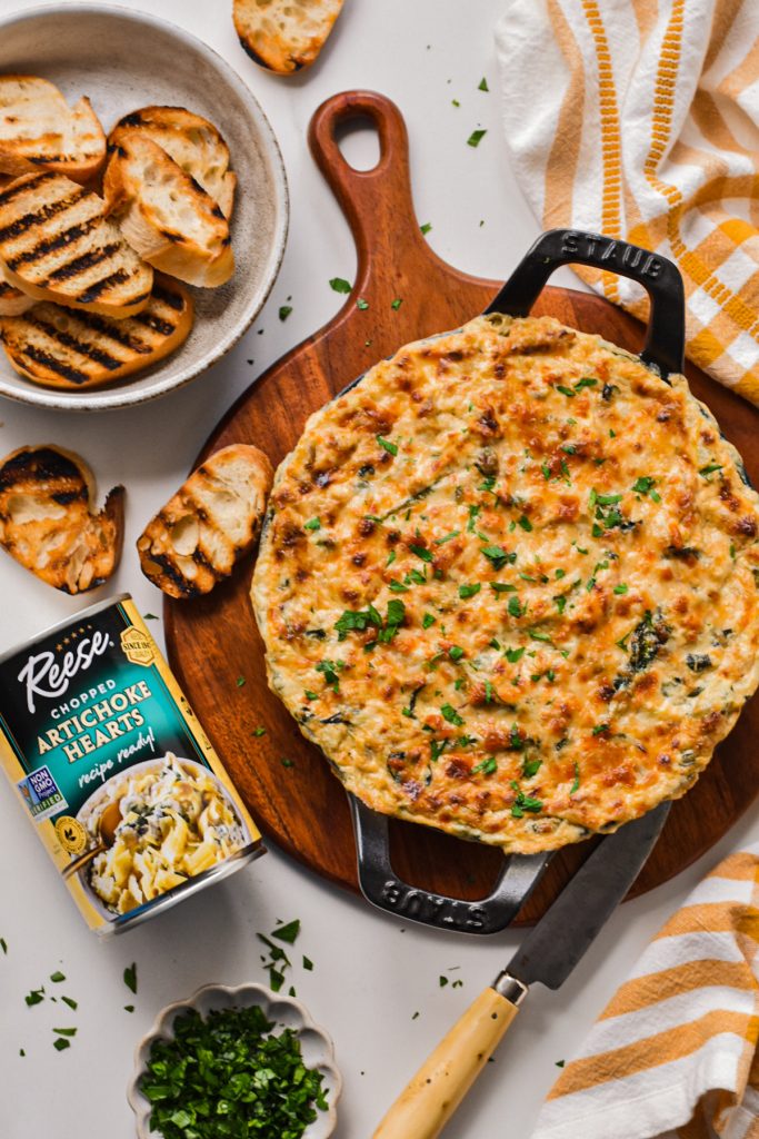 Overhead shot of Cajun spinach artichoke dip in a cast iron pan on a wooden board.
