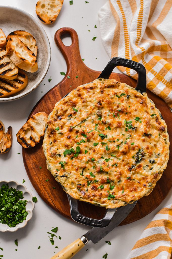 Cajun spinach artichoke dip in a cast iron skillet topped with a layer of melted cheese.