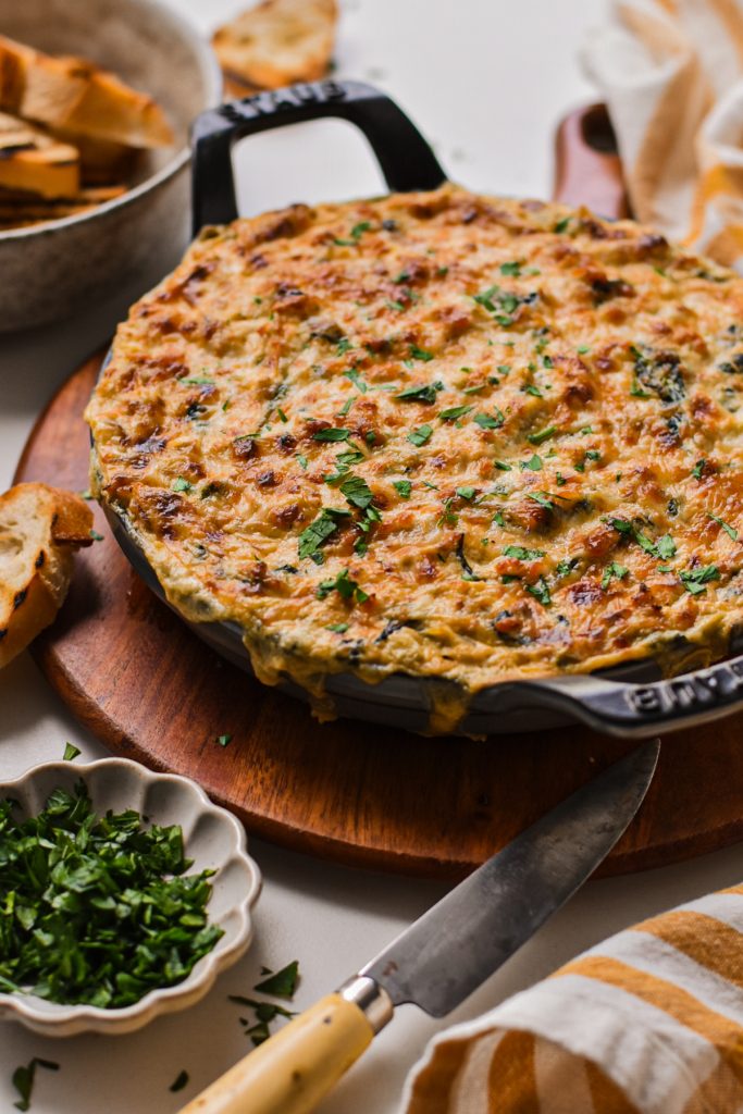 Cajun crab spinach artichoke dip served in a cast iron skillet wit melted cheese on top.