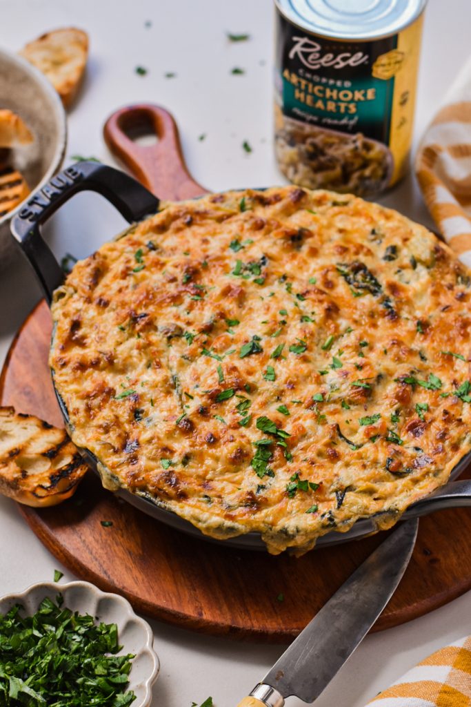 Cajun crab spinach artichoke dip in a cast iron skillet on top of a wooden board.