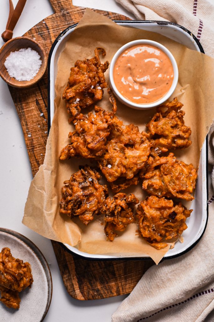 Spicy onion ring fritters on a sheet plan served with a side of dipping sauce.