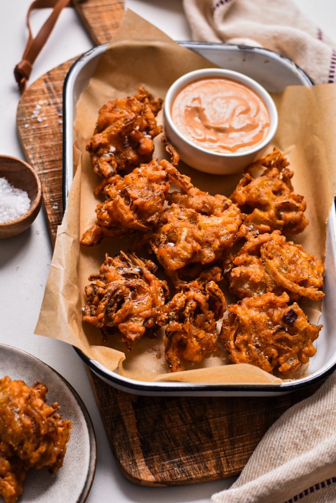 Bhaji onion fritters served on a sheet pan lined with parchment served with dipping sauce.