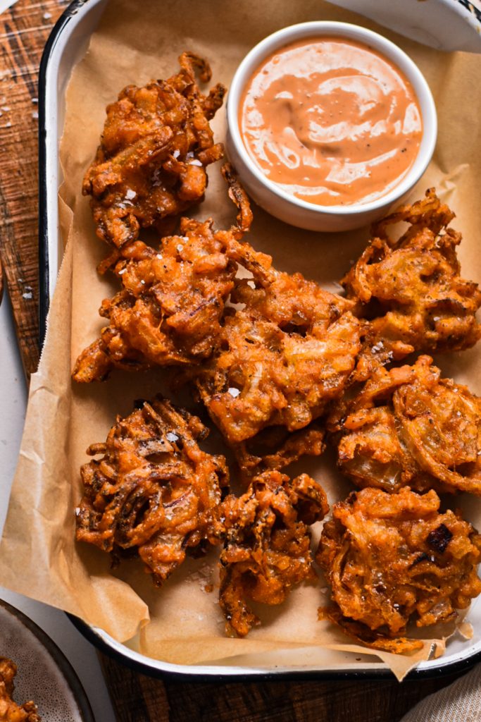 Close up of the spicy onion ring fritters on a sheet pan served with a ramekin of sauce.