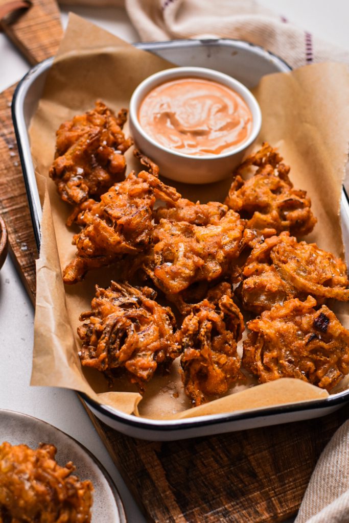 Crispy fried onion ring fritters on a small sheet pan on a wooden board.