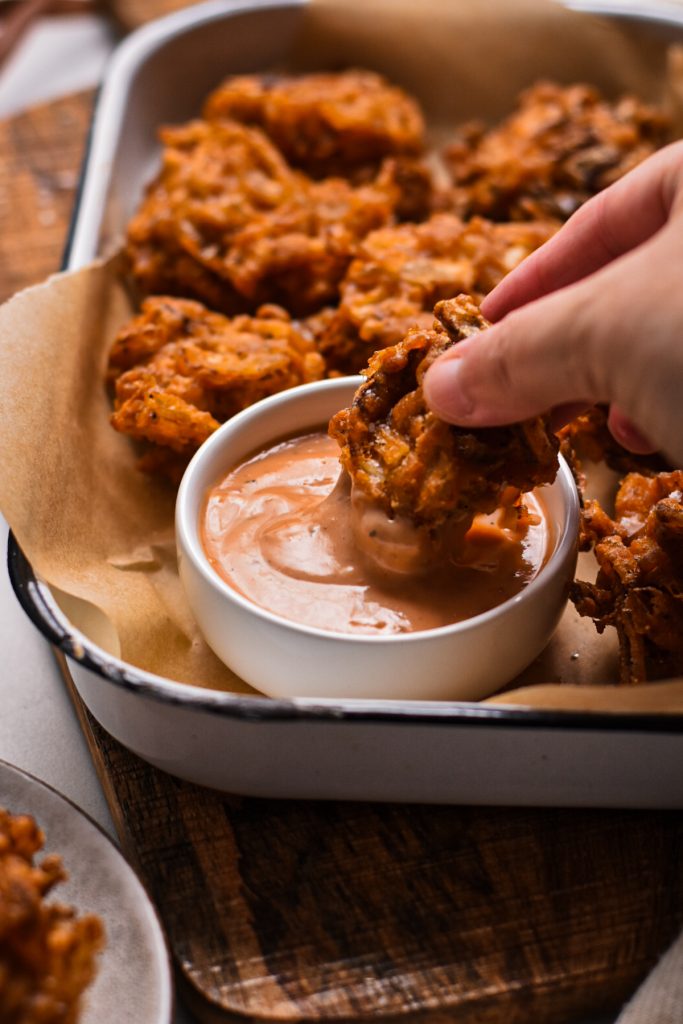 Hand dipping a spicy onion ring fritter into the ramekin of sauce.