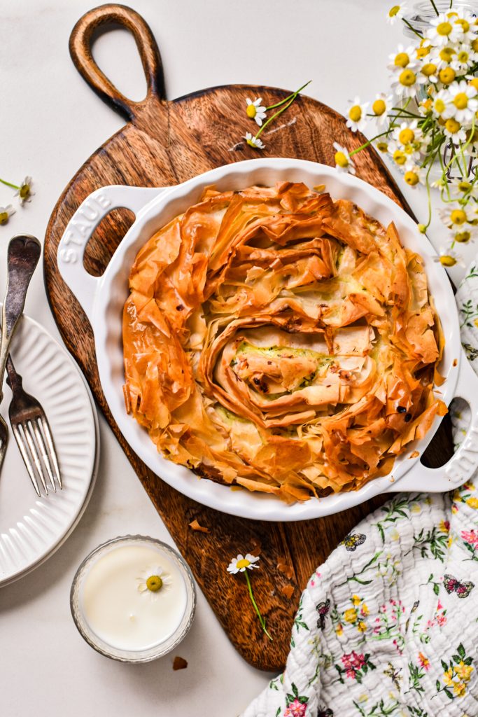 Overhead shot of baked farmer cheese phyllo pie in a white baking dish on a wooden board.