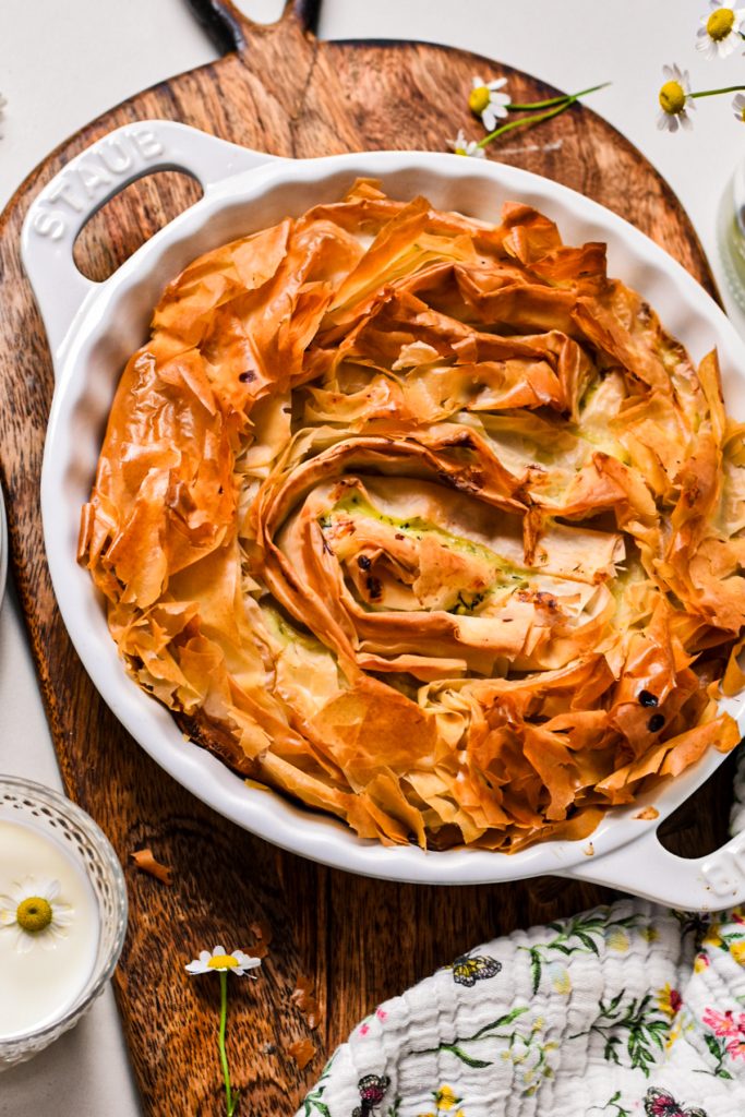 Farmer cheese phyllo pie in a white pie dish on a wooden board.