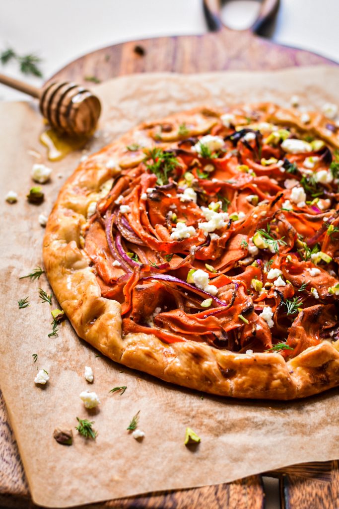 Spicy carrot and feta galette on a wooden board lined with parchment paper.