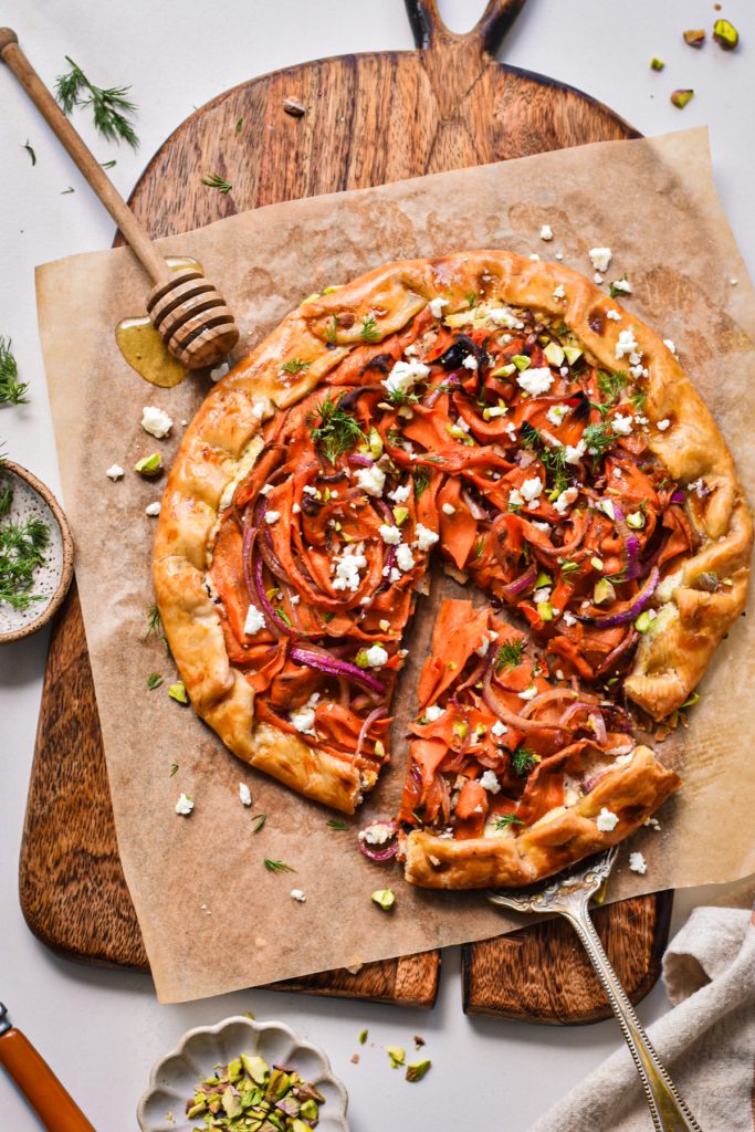 Overhead shot of spicy carrot and feta galette on a wooden board with one slice coming out on a spatula.