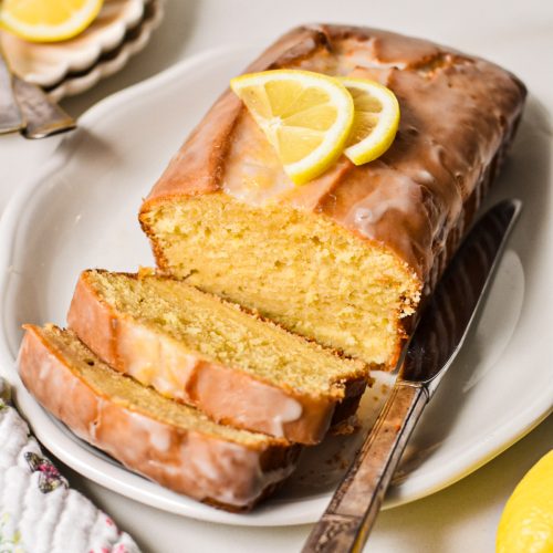 Lemon loaf cake with a glaze and fresh lemon on top with two slices off the end.