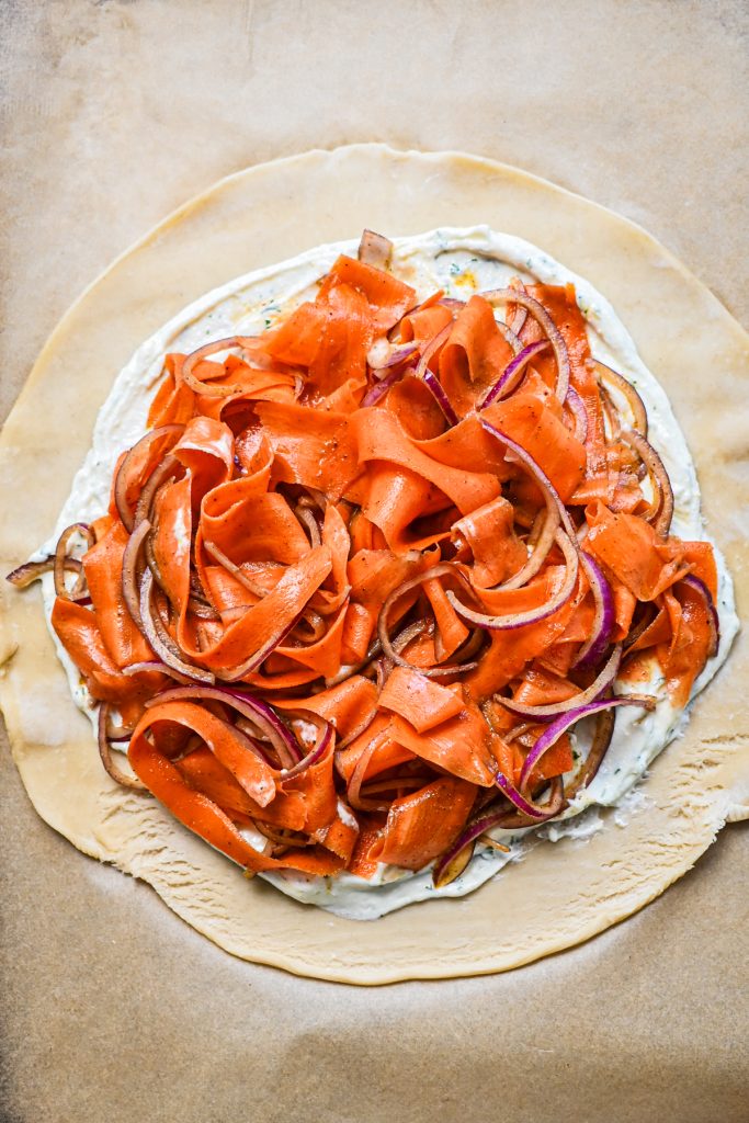 Carrot ribbon and onion mixture on top of the filling layer on a pie crust.