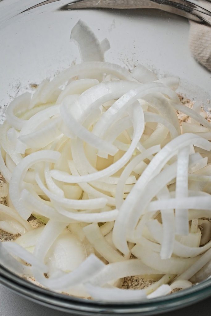 Thinly sliced onions added to the flour and spice mixture in a bowl.
