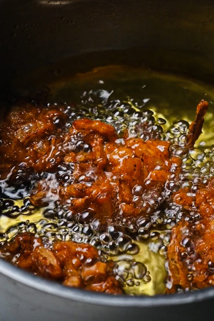 Portions of the breaded onions being fried in hot oil in a pot.