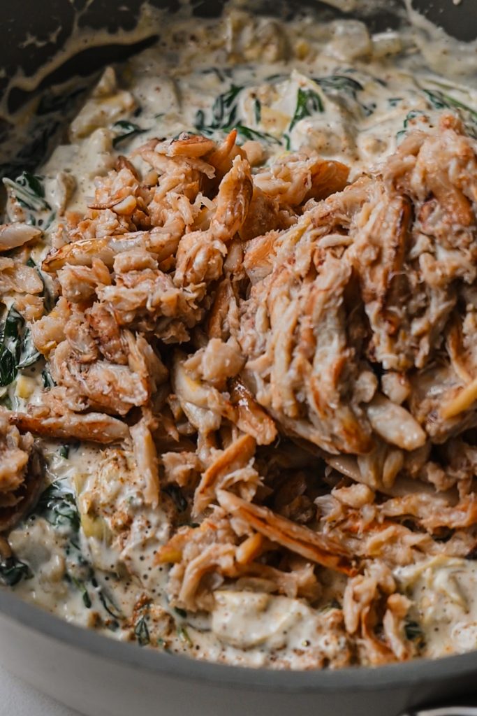 Crab meat added to the spinach artichoke mixture in a skillet.