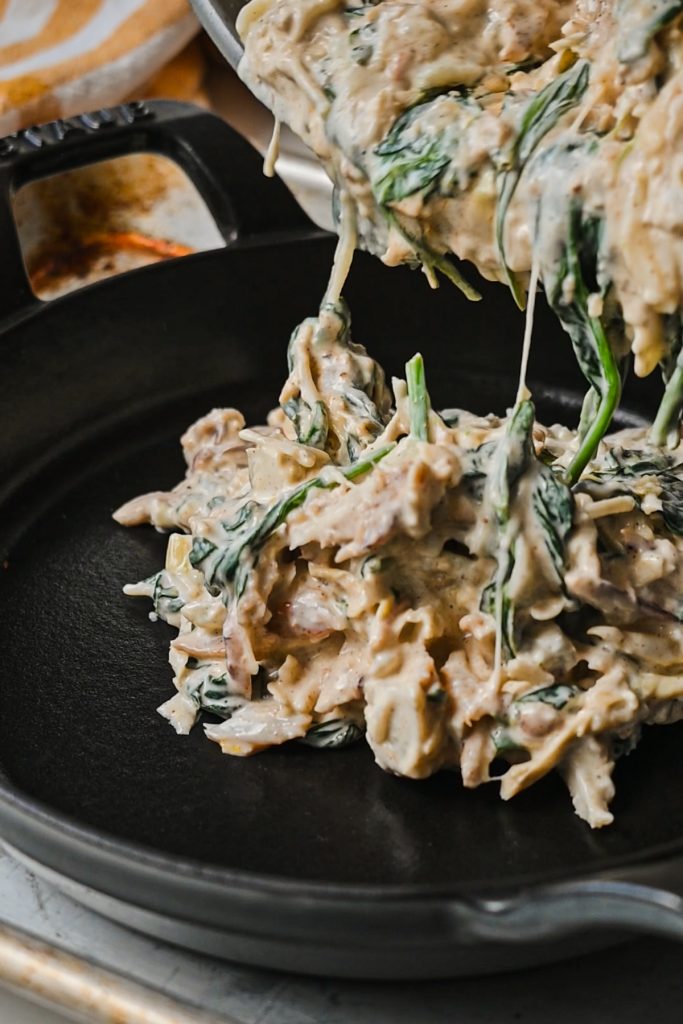 Pouring the spinach artichoke mixture into a cast iron skillet to bake.